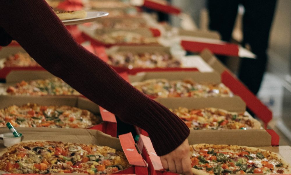 person reaching of a pizza on other side of table